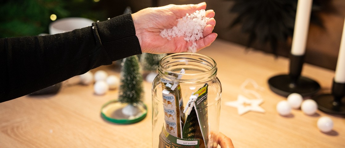 Kunstschnee wird in ein weihnachtlich dekoriertes Gurkenglas gefüllt | WestLotto Bastelidee