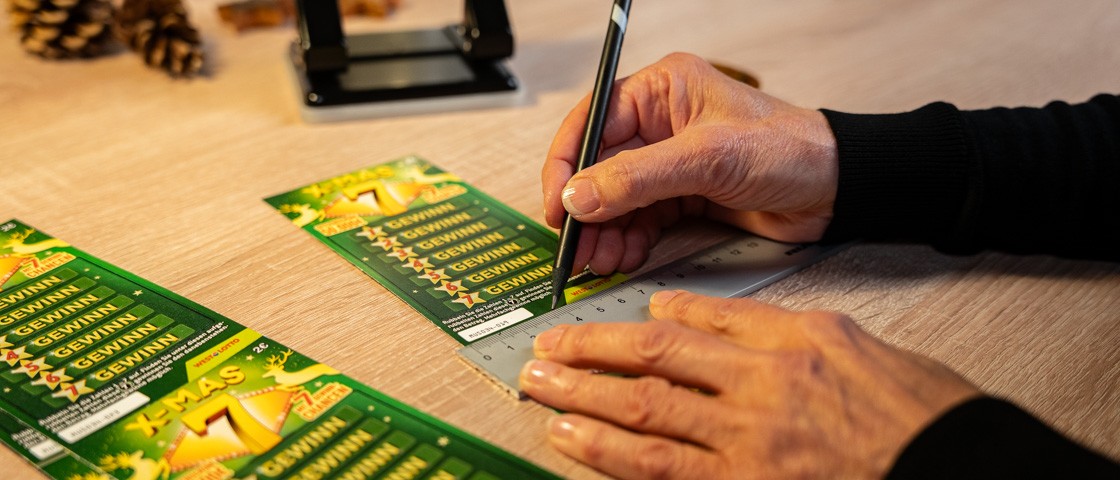 Eine Hand zeichnet mit einem Bleistift auf ein Rubbellos | WestLotto