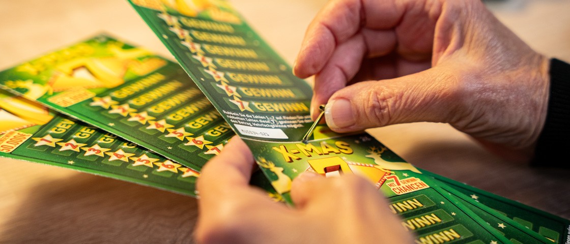 Zwei Hände stecken eine Musterbeutelklammer durch mehrere Rubbellose | WestLotto