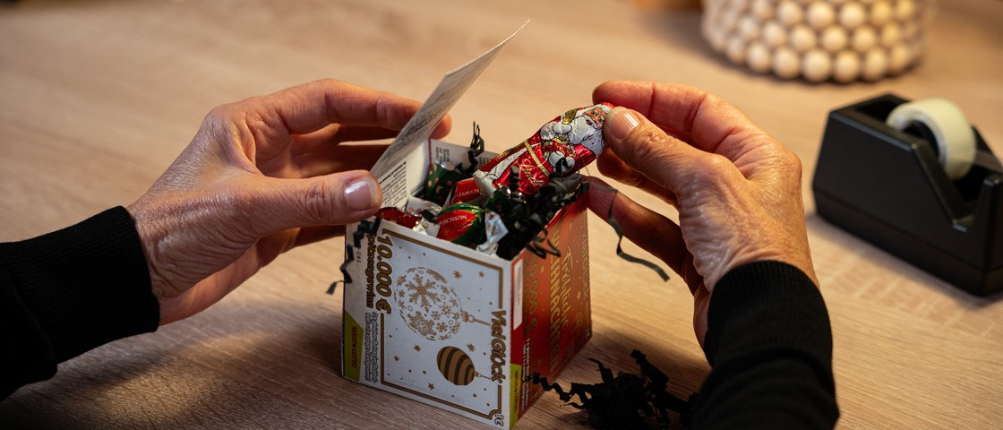 Füllmaterial und ein Schoko-Weihnachtsmann werden in einen Rubbellos-Würfel gelegt | WestLotto Bastelidee